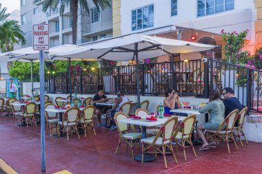 Ocean Drive boyunca yaya geçidinde bazı masalarla restoranda oturan insanların görüntüsü. Miami Beach 'te güneşli bir yaz günü. ABD. 