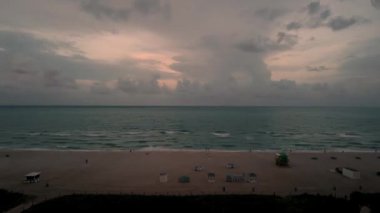 Miami Plajı 'nda gün batımının muhteşem videosu. Solgun gökyüzünde hareket eden bulutlar ve Atlantik Okyanusu ufka doğru birleşiyor.. 