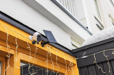 Close-up view of exterior surveillance camera equipped with solar panel installed on facade of villa on frosty winter day. Sweden. clipart