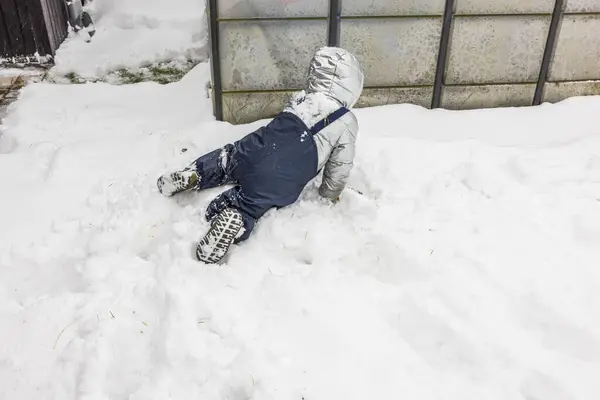 View of a child playing in the snow in the garden on a chilly winter day. Sweden.