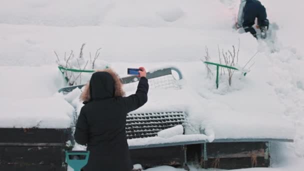 一个女人在雪地覆盖的后院用手机录下她儿子的视频的照片 — 图库视频影像