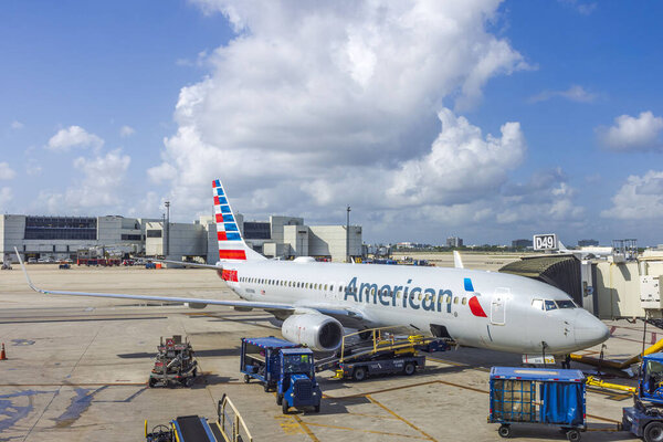 Вид припаркованных самолетов American Airlines в аэропорту, подключенных к реактивному мосту для посадки пассажиров и погрузки багажа в грузовые отсеки. Майами. США. 