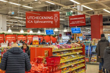 Bir İsveç ICA süpermarketinin iç manzarası. Çeşitli mallarla dolu rafların yanında müşteriler var. İsveç. 
