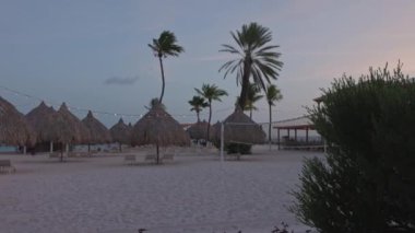 Kumlu plajlı, kumlu bir otelin gün batımında güzel bir manzara, palmiye yapraklı şemsiyeler, ve Karayip Denizi kıyıları boyunca uzanan güneş pansiyonları. Curacao.