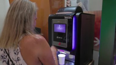 Kadının oteldeki bir kafe makinesinden kağıt bardağa kahve doldurduğu yakın çekim görüntüsü. Miami Plajı. ABD. 