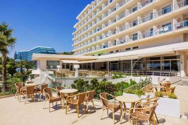 Açık hava oturma alanı olan pitoresk bir otel dış görünüşü, konuklar için masalar ve sandalyeler, parlak güneşli bir günün arka planına kurulmuş. Rodos. Yunanistan
