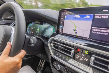 Otoyolda sürerken BMW iX3 M elektrikli aracının içindeki cihaz panelinin ve navigasyon ekranının yakın görüntüsü. 