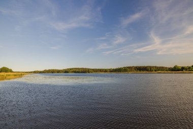 Gölün dingin gökyüzünün güzel manzarası ufuktaki uçsuz bucaksız mavi gökyüzü ile pürüzsüz bir şekilde birleşir. İsveç.