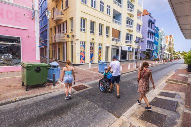 Curacao 'da manzaralı bir caddeden geçen insanların görüntüsü, tekerlekli sandalye süren bir adam da dahil.. 