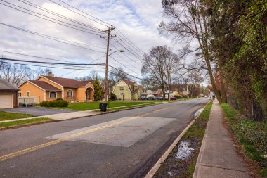 Tepemizde elektrik hatları, kaldırımlar ve arka planda ağaçlar ve bulutlu bir gökyüzü olan çeşitli evler olan bir yerleşim yeri manzarası. New Jersey 'de. ABD.