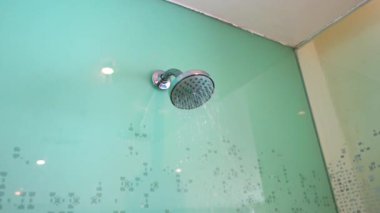 Duvara monte edilmiş duş başlığından gelen su akışının yakın görüntüsü otel banyosu, şeffaf bir cam bölmeyle ayrılmış.. 