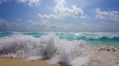 Karayip Denizi 'nin muhteşem mavi dalgalarının güzel manzarası Meksika bulutlarıyla dolu engin mavi gökyüzünün altında kumlu kıyıya çarpar..