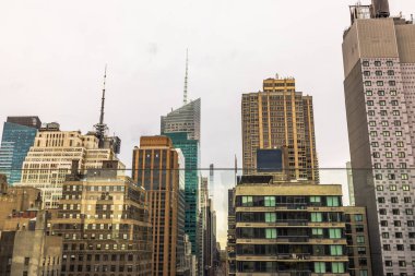 New York 'ta yoğun bir şehir siluetinin panoramik görüntüsü, bulutlu bir gökyüzü altında modern cam gökdelenler ve geleneksel mimarinin bir karışımını sergiliyor. New York. 
