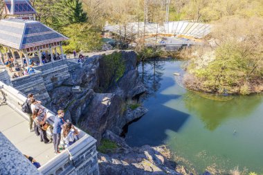 Güneşli bir günde sakin bir gölet ve kayalık uçurumlara bakan Central Park 'taki Belvedere Kalesi' ndeki ziyaretçilerin manzarası. - New York. ABD. 