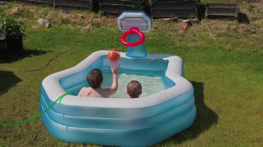 Açık havada şişme havuzda eğlenen iki çocuk, arka bahçede yaz güneşinin altında su basketbolu oynuyorlar. İsveç.