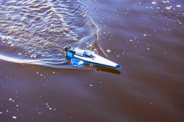 Uzaktan kumandalı mavi ve beyaz bir sürat teknesinin yakın görüntüsü sakin suda hareket ederken dalgalanmalar yaratıyor. İsveç.