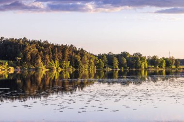 Gölde gün batımının güzel bir görüntüsü ve orman ağaçlarının yansıması. İsveç.