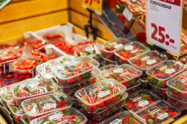 Bir süpermarketin üretim reyonundaki plastik kaplarda paketlenmiş çilek bulunan bölümün yakın görüntüsü. 