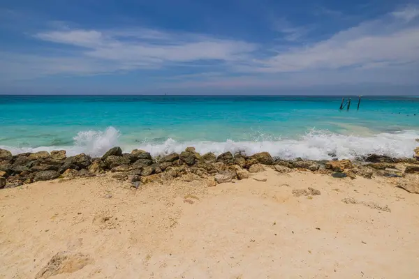 stock image Beautiful view of waves from the Caribbean Sea rolling onto a sandy beach protected by stones. Aruba.