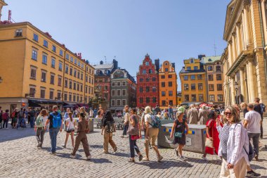 Stockholm 'de renkli tarihi binalar ve kaldırım taşı sokaklarda yürüyen insanlarla dolu hareketli bir kasaba meydanı manzarası..
