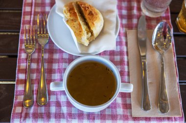 Bir kase çorba, tabakta bir parça ekmek ve kırmızı ve beyaz kareli masa örtüsüne yerleştirilmiş çatal bıçak seti. Curacao.