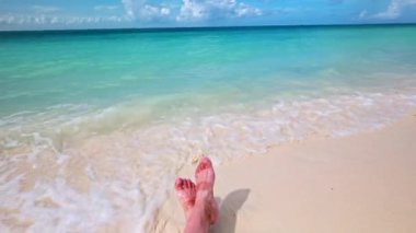 Aruba 'da kumlu sahilde turkuaz deniz dalgaları tarafından yıkanan sandaletlerin ayak izleriyle yakın çekim görüntüsü..