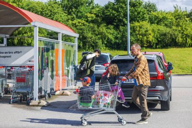 Güneşli bir günde otoparkta iki çocukla alışveriş arabasını iten bir adam.. 
