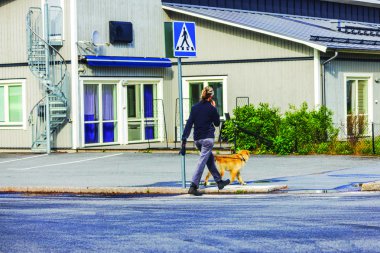 Bir adam yaz günü köpeğini sarmal merdivenleri olan bir apartmanın yakınında gezdiriyor. İsveç.