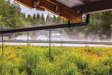 View from under the roof of a building onto a highway with moving cars after a summer rain, where steam rises from the sun-heated asphalt. Sweden. clipart