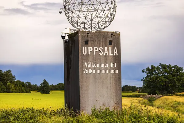 stock image Uppsala welcome sign in Swedish countryside with green fields and trees in background on cloudy blue sky backdrop.