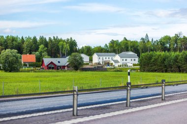 Çağdaş villaları olan verimli tarım alanları ve pitoresk köylerle çevrili, şeritleri ayıran tel bariyerlerle çevrili manzaralı otoyol. İsveç.