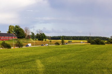 Buğday ve çavdar tarlaları arasında hareket halindeki trafiğin orman zeminine kurulduğu güzel bir otoban manzarası. İsveç.