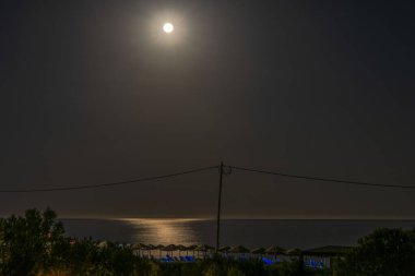 Akdeniz 'i aydınlatan ay ışığı ile gece kumsalının sakin manzarası su yüzeyinde parıldayan bir ışık yoluydu. Yunanistan.