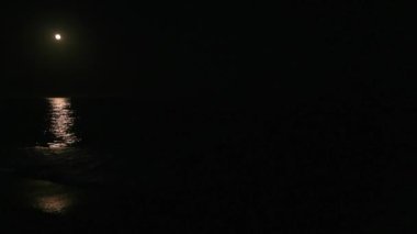 Gece Akdeniz 'de dalgalar yavaşça sahili kaplıyor, dolunay kıyıya doğru parlak bir yol açıyor. Girit.