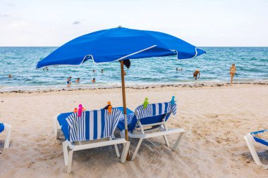 Şezlonglu kumsal, plaj havluları plaj klipsleri, şemsiyeler ve güneşli bir günde Atlantik Okyanusunda yüzen insanlar. Miami Plajı. ABD. 