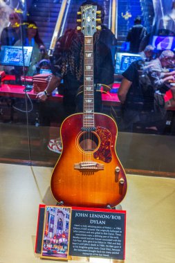 Guitar on display at Hard Rock Cafe in Manhattan, featuring John Lennon and Bob Dylan, with plaque detailing history of 1966 Gibson G-160E Acoustic. New York. USA. clipart