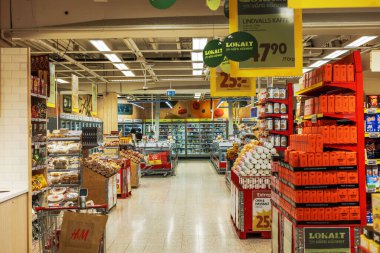 Aisle in grocery store filled with various products, including packaged goods and fresh items, along with promotional signs and shopping carts. clipart