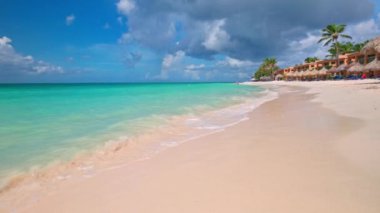 Otel manzaralı Karayipler sahilinde turkuaz dalgalarla kumlara uzanmış bir adam ayaklarına hafifçe dokunuyor. Aruba.