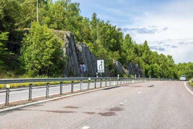 Kayalık dağ ve orman zeminine karşı yol daraltıcı işaretli otoban. İsveç. Uppsala. 
