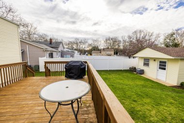 Modern villanın arka bahçesindeki verandanın yakın görüntüsü. Açık mobilya, barbekü ve bulutlu gökyüzüne karşı bahçe kulübesi. ABD.