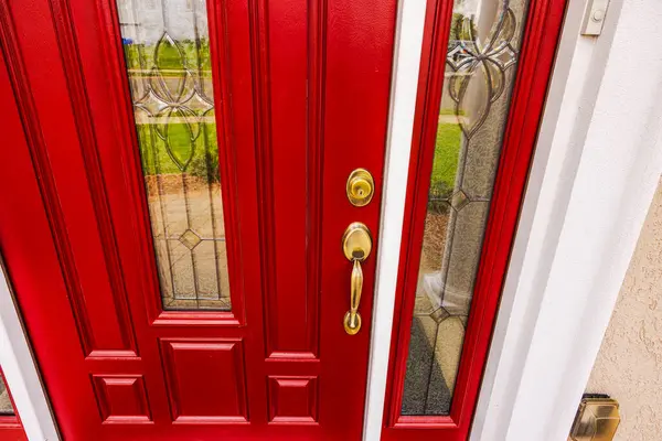 Stock image Close-up of a red oak entry door with glass inserts featuring floral patterns, golden lock, and handle. USA.