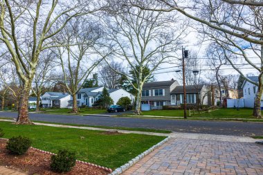 Bir ve iki katlı villaları, yeşil çimenleri ve bulutlu gökyüzünün altında asfalt yolu olan sakin bir banliyö mahallesinin bahar günü manzarası. New Jersey, ABD. 