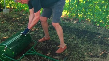 Çimen toprağı taradıktan sonra üst kattaki toprak artıklarını boşaltan adamın yakın çekimi. İsveç.