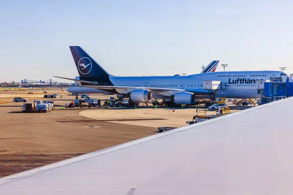 stock image View from airplane window of parked Lufthansa Boeing 747 on the runway, with passengers boarding and luggage being loaded. New York. USA. 