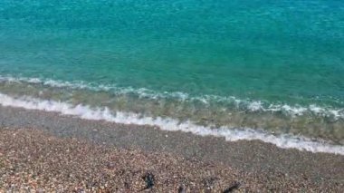 Yumuşak mavi Akdeniz dalgalarının yakın çekimi çakıllı kumsala çakıl taşları ve sudan yansıyan gümüş rengi ile hafifçe vuruyor. Yunanistan.