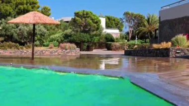 Otellerin açık havuzun yakın görüntüsü sert rüzgarlar altında, su Girit Adası 'ndaki sallanan tropik ağaçların arka planına karşı terası turluyor. Yunanistan.