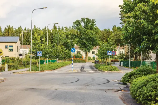 stock image View of quiet residential street with greenery, road signs, and houses in background on sunny summer day. Sweden, Europe.