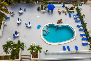 Açık yüzme havuzu, güneş pansiyonları, şemsiyeler ve yüzen insanların olduğu otel manzarası. Miami Plajı. ABD.