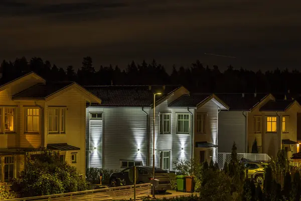 stock image Night suburban neighborhood view with modern homes illuminated by warm and cool lighting. Quiet residential street under dark sky. Sweden.