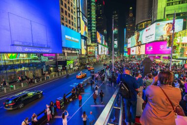 Times Meydanı 'nın yoğun gece manzarası, büyük reklam panoları, parlak ışıklar ve New York' ta kırmızı merdivenlerde duran insanlar. ABD.